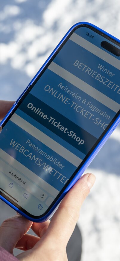 Ein Frau hält ein Handy in der Hand und hat die Homepage der Reiteralm geöffnet. | © Lorenz Masser