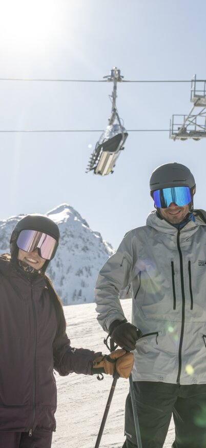 2 Skifahrer stehen auf der bestens präparierten Piste der Reiteralm. Im Hintergrund fährt ein Sessel der Schoberbahn. | © Lorenz Masser
