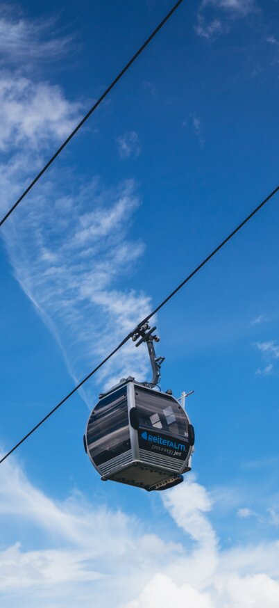 Blauer Himmel mit Wolken und in der Mitte eine Gondelkabine vom Preunegg Jet der Reiteralm.